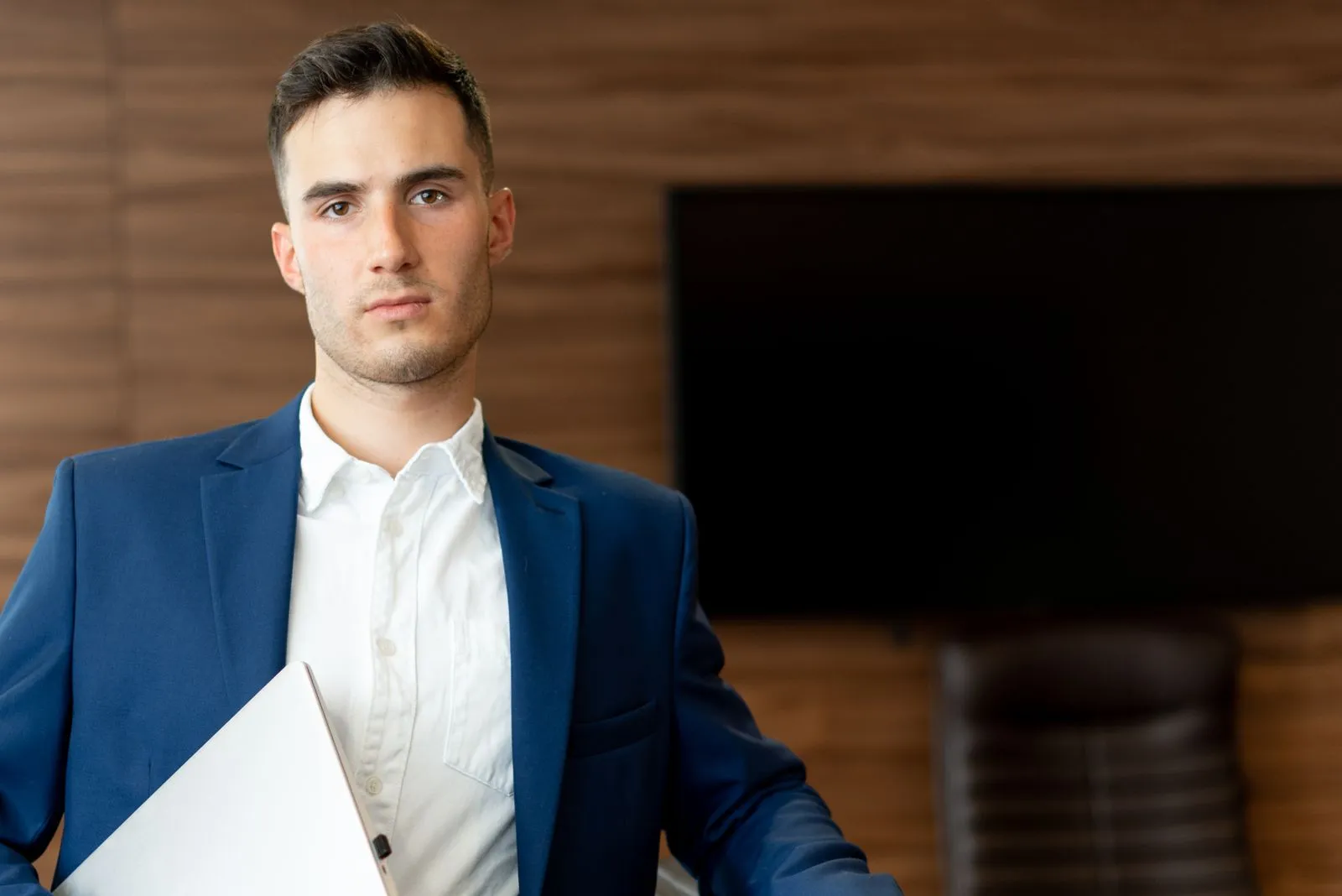 Confident young man in a blue suit holding a laptop, asking if you can make $200,000 in cybersecurity