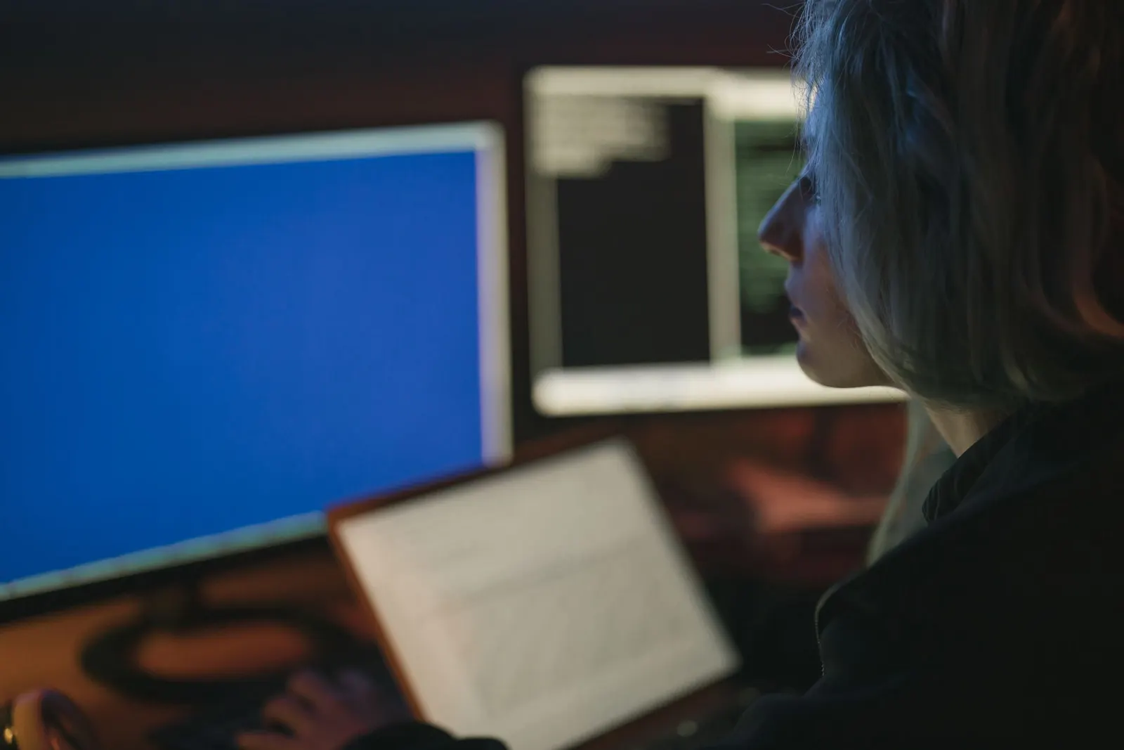 A security analyst working across several monitors of code at night, a typical cybersecurity career