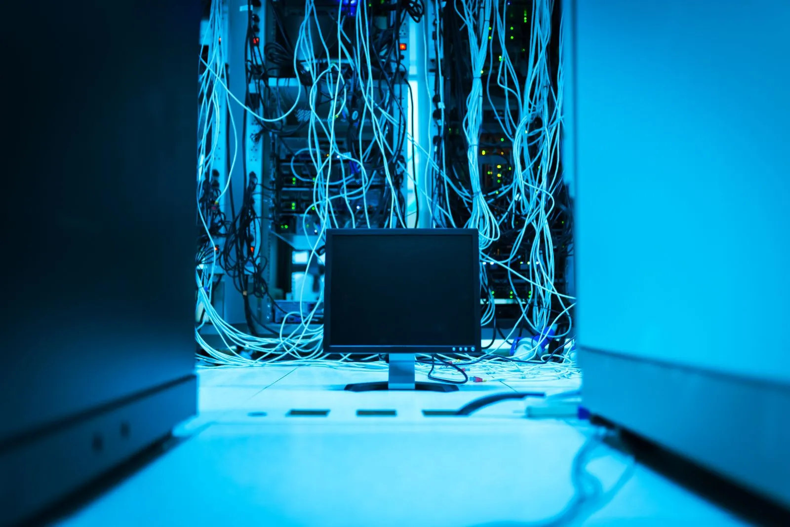 Dense network cabling hanging from server racks behind a monitor in a data center that architects design