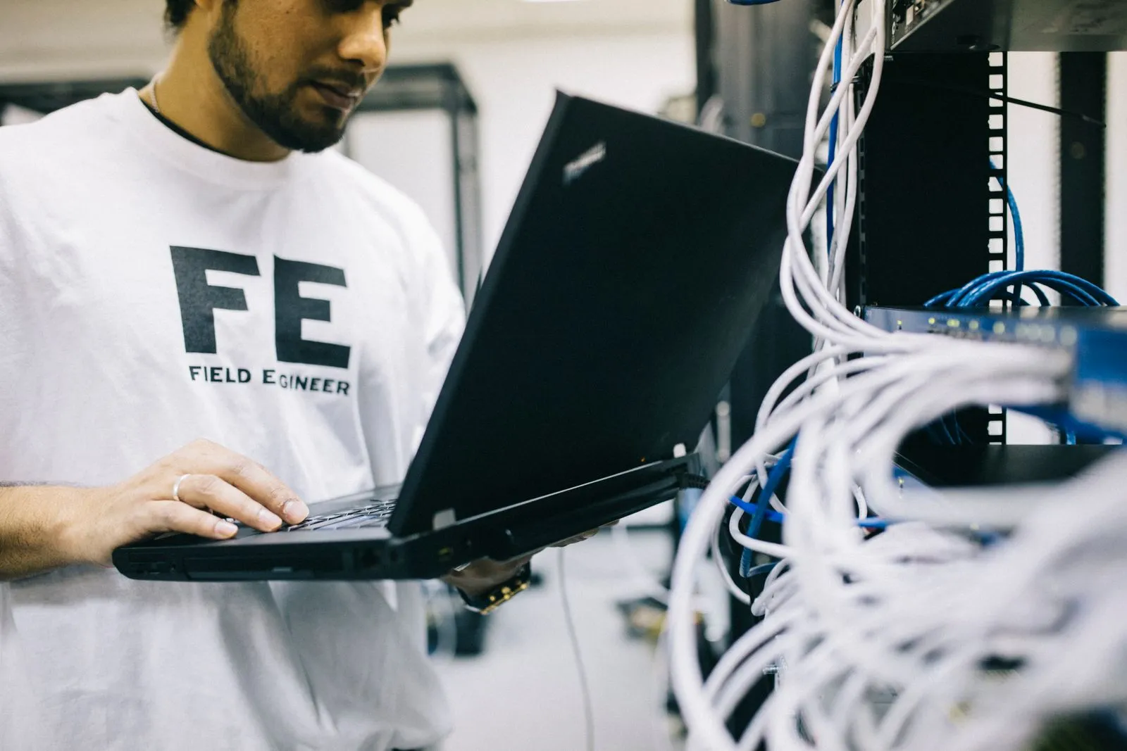 Network engineer holding a laptop beside a server rack of patch cables while planning a network build