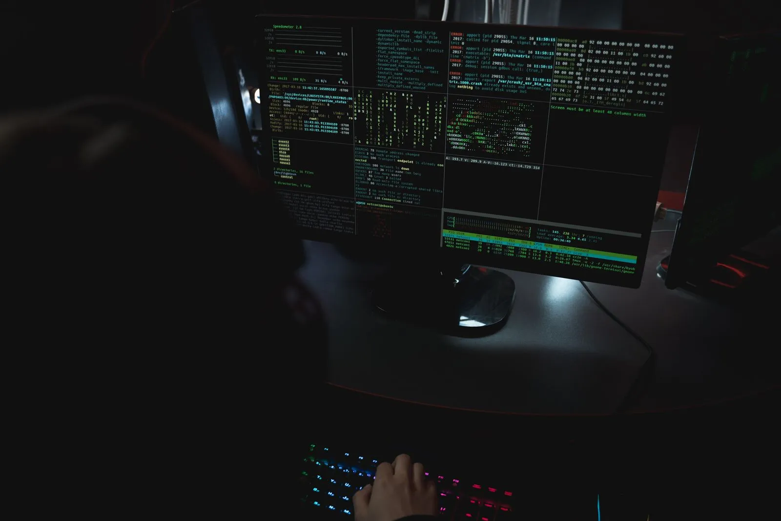 Cybersecurity analyst reading lines of code across several monitors in a dark office