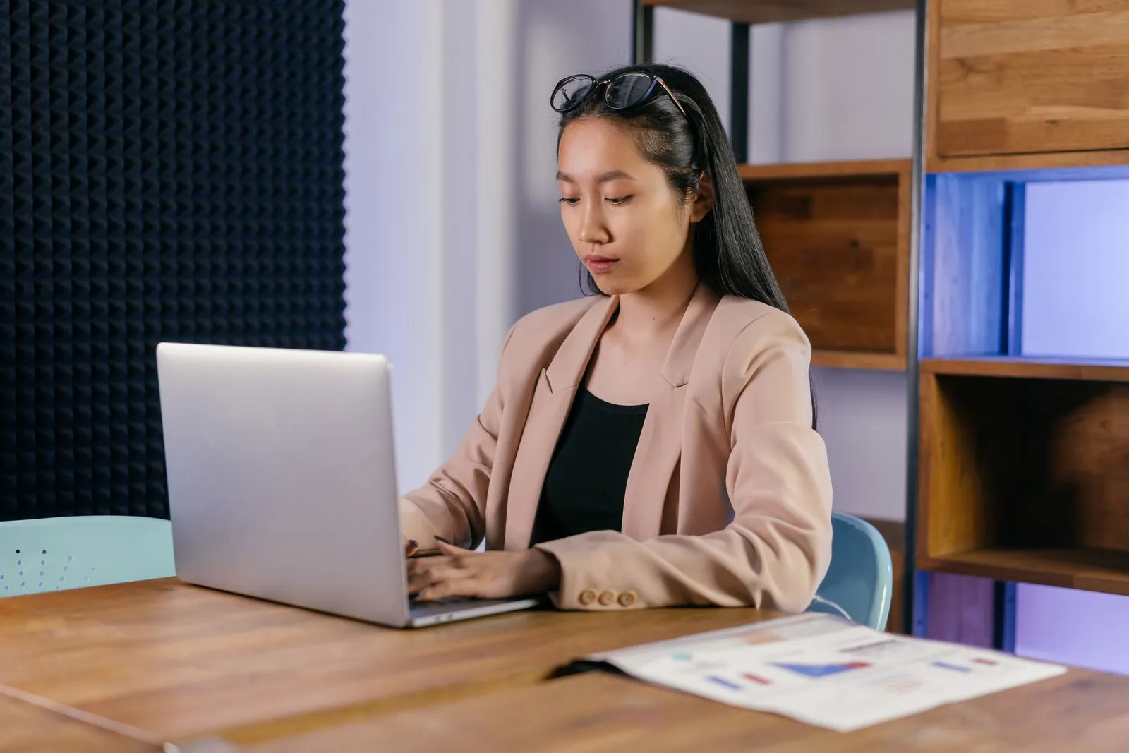 Woman reviewing printed charts beside her laptop while checking cybersecurity salary ranges
