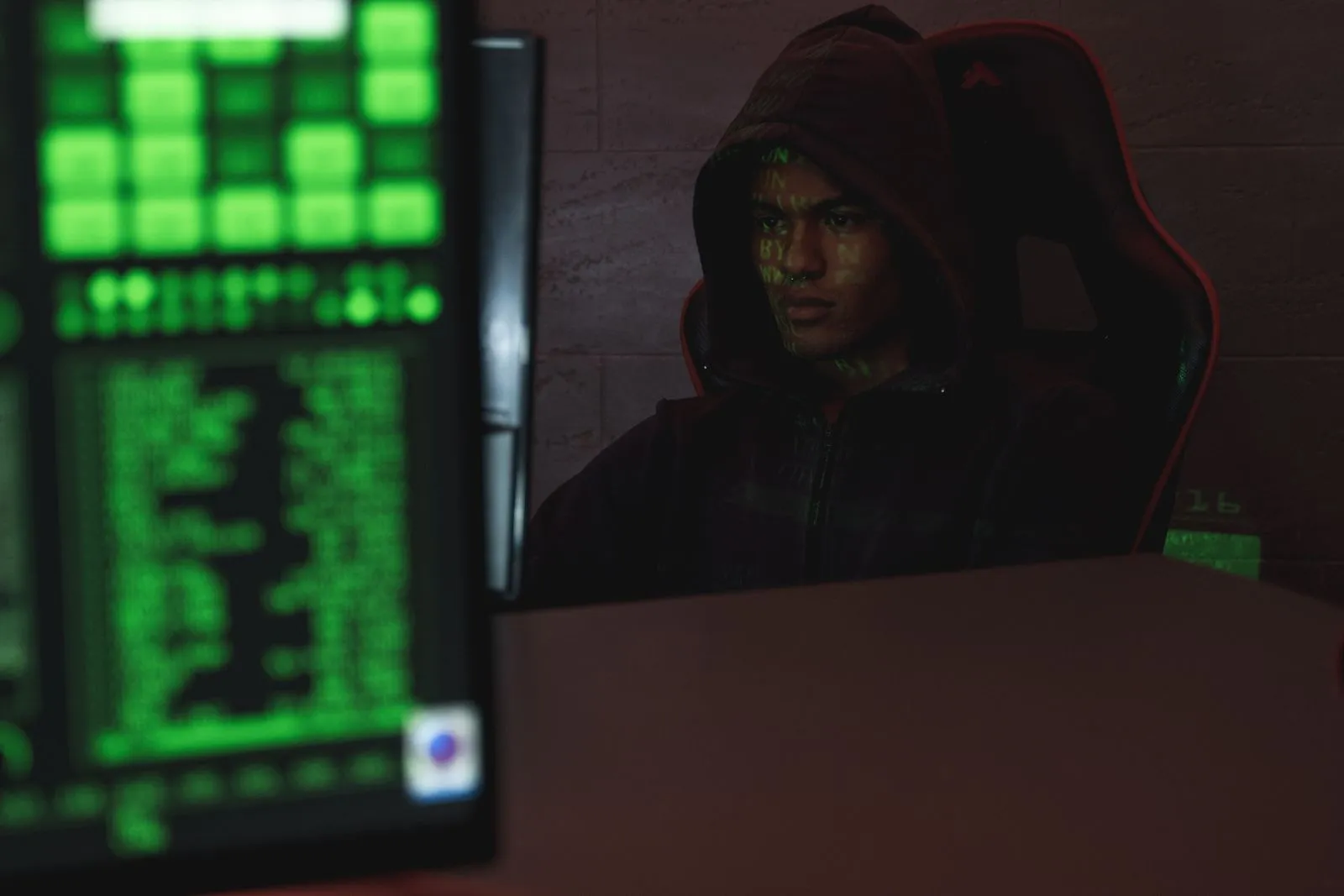 Hooded newcomer typing at a keyboard in a dark room while studying entry-level cybersecurity skills
