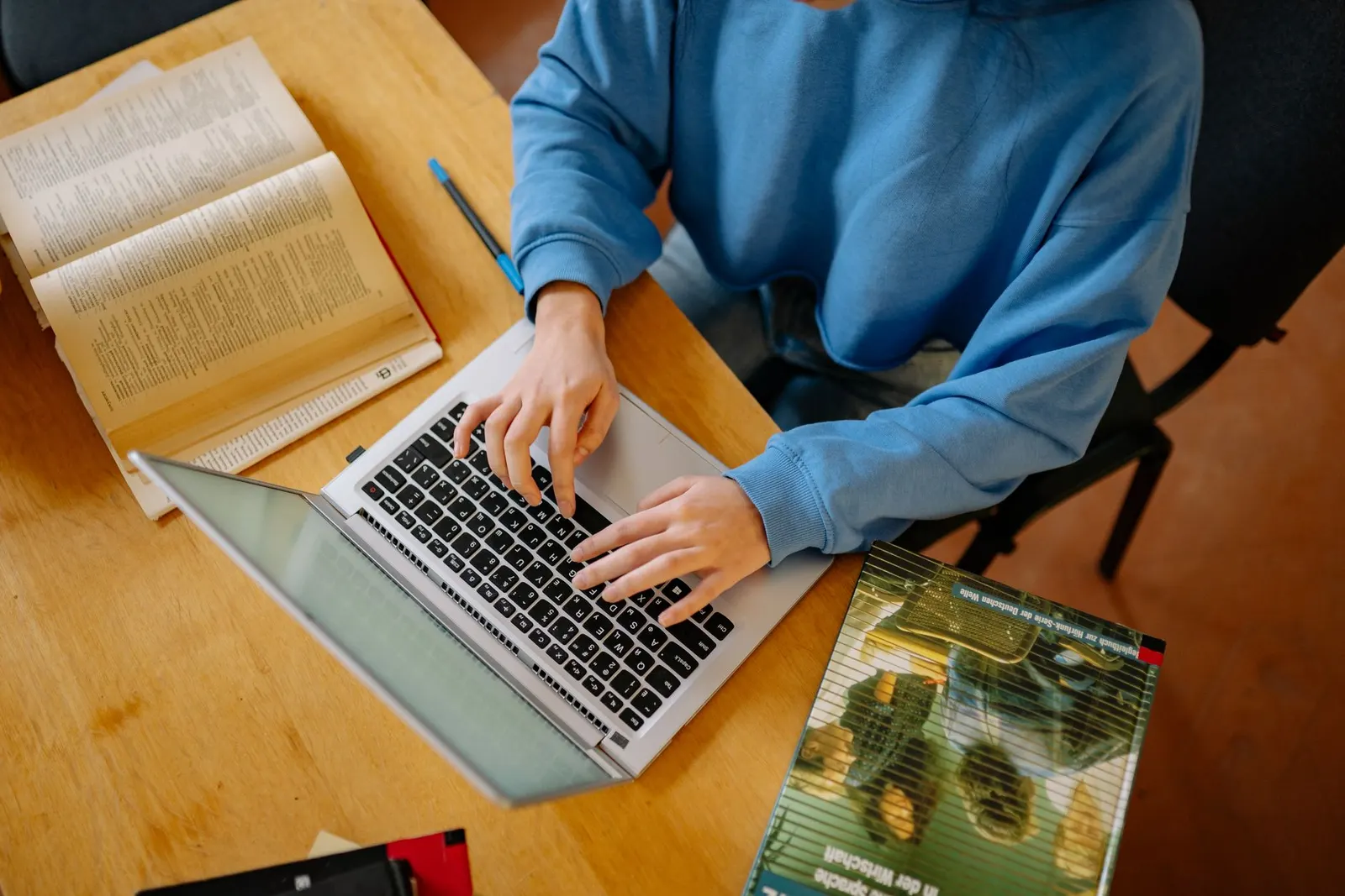 A student typing on a laptop beside open books while working through an online cybersecurity degree guide