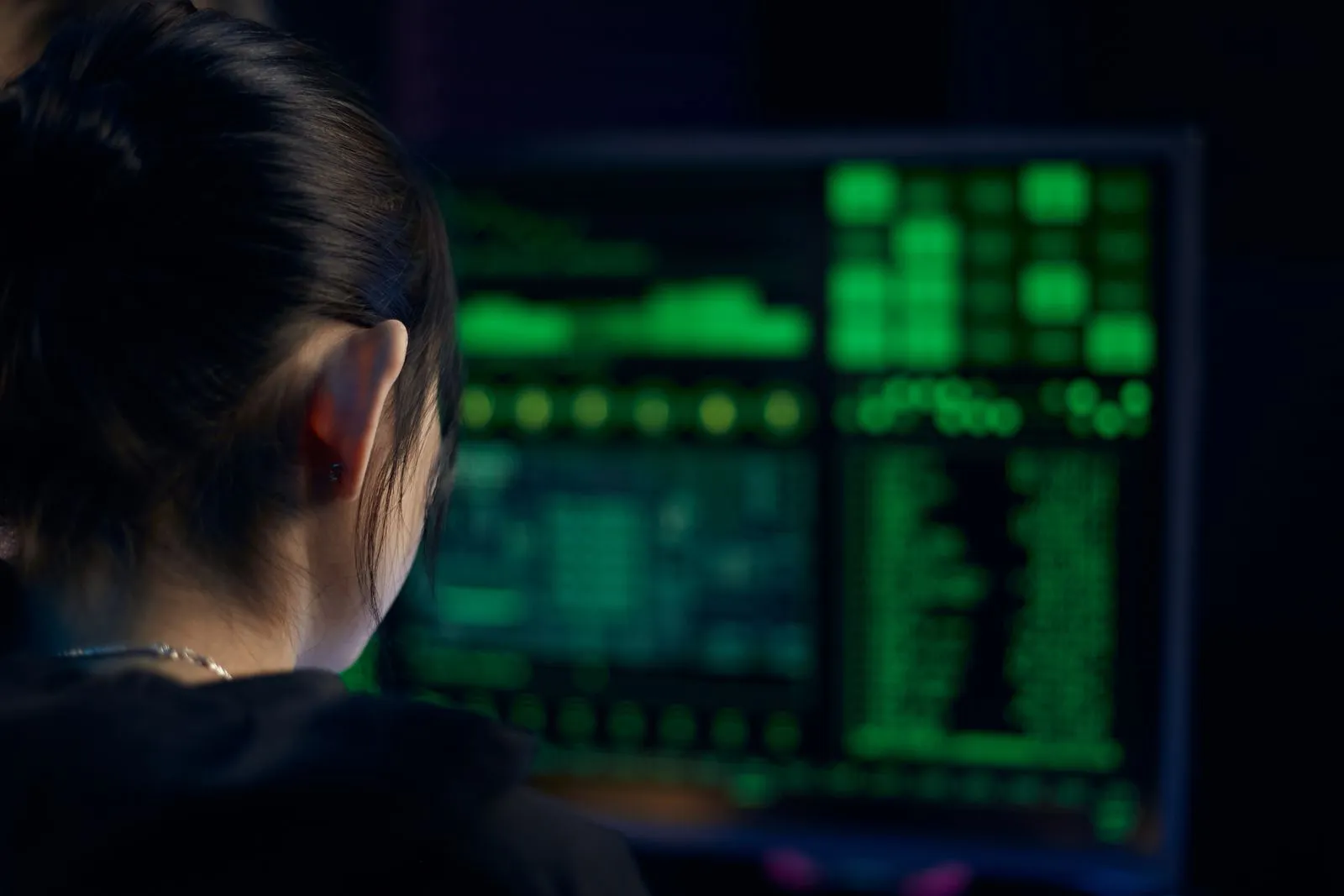 Woman studying data on a monitor in a dark room while working as an information security analyst