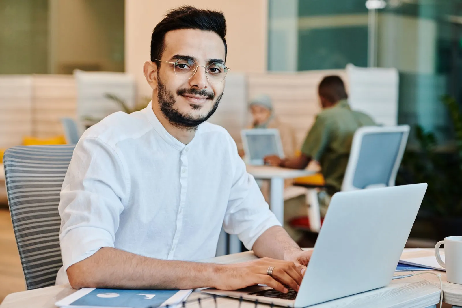 Man in glasses using a laptop in a bright workspace while weighing a cybersecurity degree