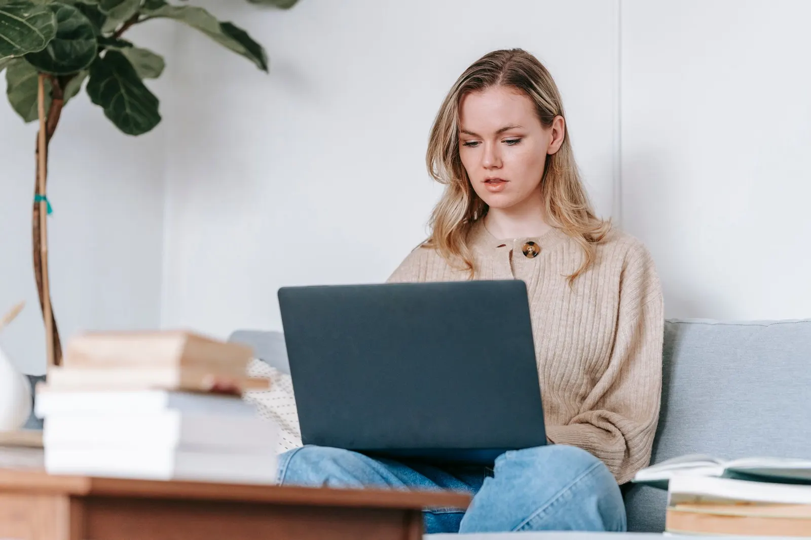 A woman comparing online cybersecurity program rankings on a laptop from her sofa at home