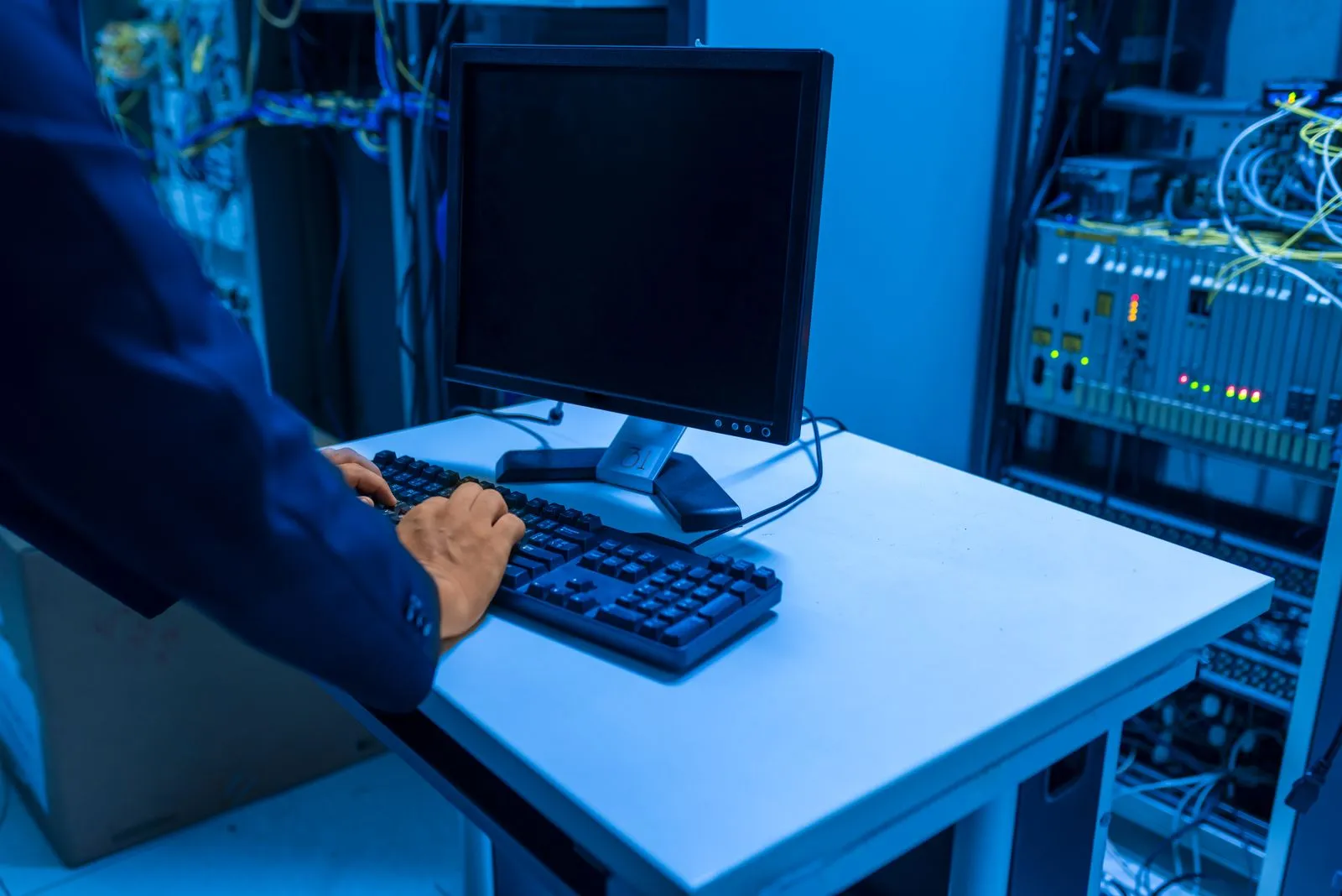 IT technician working at a computer in a blue-lit server room as a systems administrator